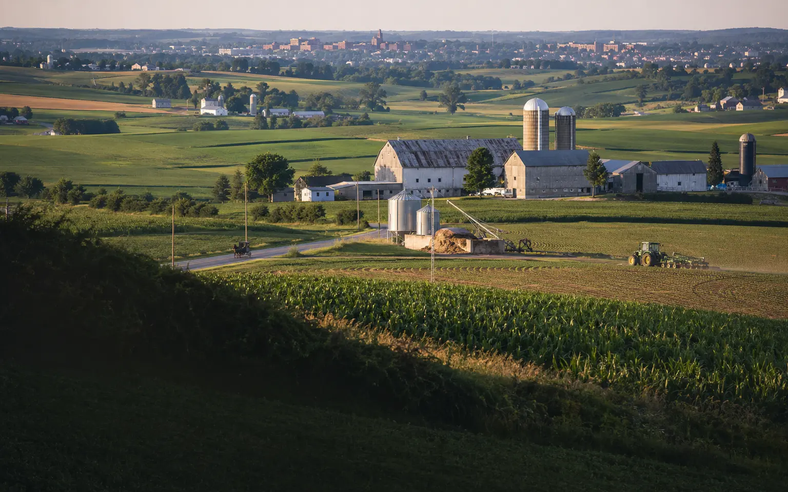 Conceptual editorial Lancaster County scene with working fields, limestone farm buildings, and a market-city edge